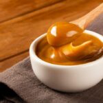 Imagem de um pote pequeno de doce de leite com uma colher pegando uma porção