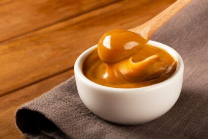 Imagem de um pote pequeno de doce de leite com uma colher pegando uma porção