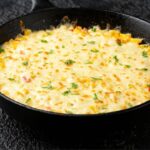 Foto mostra um omelete de legumes na frigideira em cima de uma bancada de mármore.