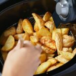 Batata rústica dentro da air fryer. Uma mão colocando sal na batata.