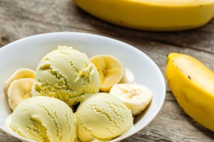 Foto mostra sorvete de banana num pote com bananas in natura ao lado em cima da mesa.