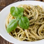 Foto mostra macarrão alho e óleo dentro de um prato branco em cima de uma mesa.