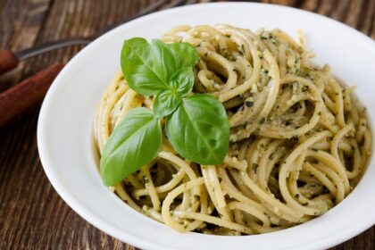 Foto mostra macarrão alho e óleo dentro de um prato branco em cima de uma mesa.