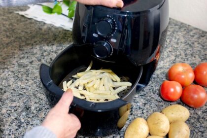 Foto mostra uma mão manuseando a air fryer com batata frita dentro.