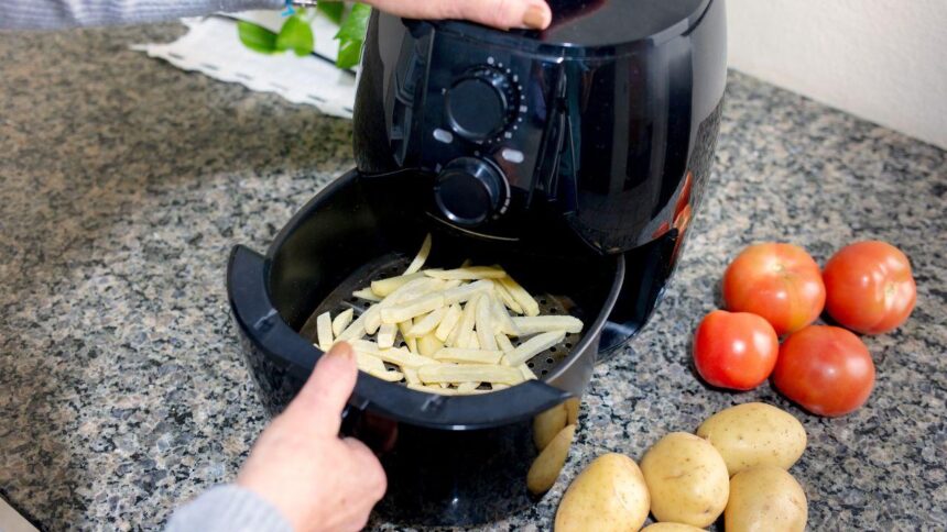 Foto mostra uma mão manuseando a air fryer com batata frita dentro.