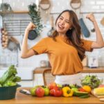 Imagem de uma mulher comemorando na cozinha, com frutas e legumes na bancada
