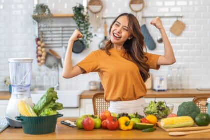 Imagem de uma mulher comemorando na cozinha, com frutas e legumes na bancada