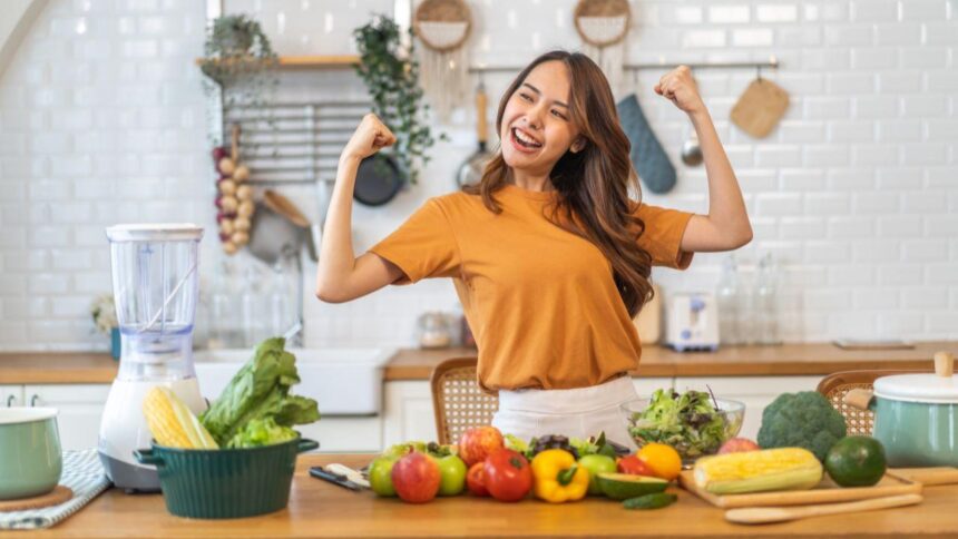 Imagem de uma mulher comemorando na cozinha, com frutas e legumes na bancada