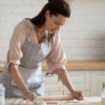 Mulher enrolando massa em uma bancada.