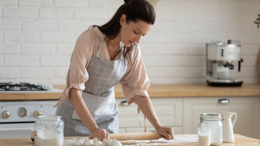 Mulher enrolando massa em uma bancada.