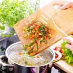 Pessoa jogando legumes em panela com água fervente