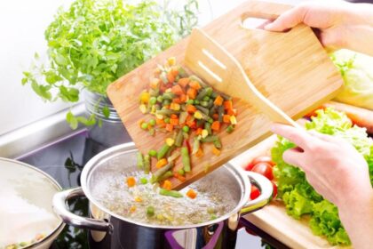 Pessoa jogando legumes em panela com água fervente
