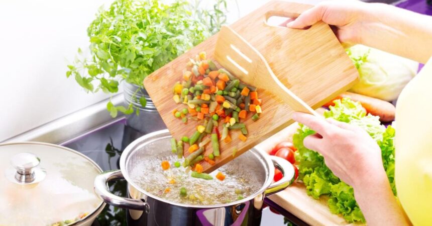 Pessoa jogando legumes em panela com água fervente