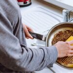 Foto de uma pessoa lavando uma frigideira com bastante resíduos