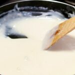 Panela de ferro com molho branco e colher de pau.