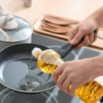 Foto mostra uma mão colocando óleo na frigideira que está e cima de um fogão por indução.