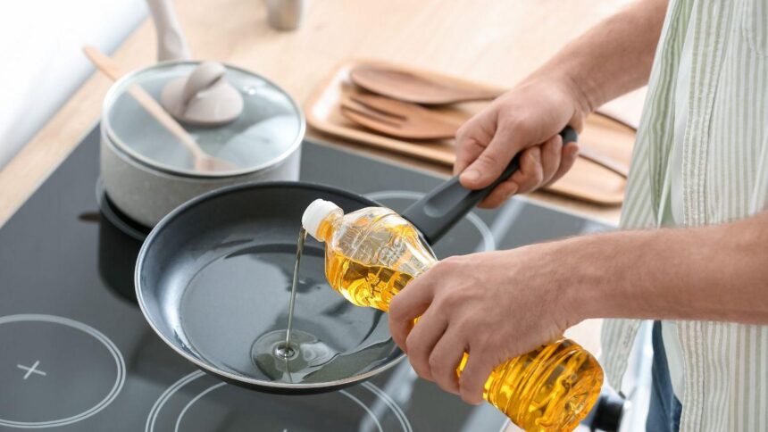 Foto mostra uma mão colocando óleo na frigideira que está e cima de um fogão por indução.