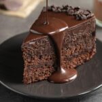 Foto mostra um pedaço de bolo de chocolate com cobertura caindo em cima.