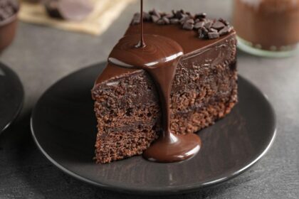 Foto mostra um pedaço de bolo de chocolate com cobertura caindo em cima.