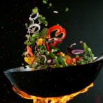 Imagem de legumes sendo flambados em uma frigideira preta