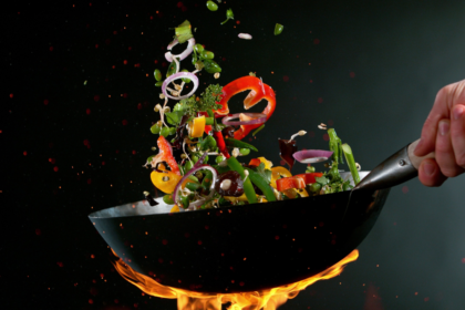 Imagem de legumes sendo flambados em uma frigideira preta