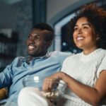 Imagem de um casal comendo pipoca enquanto assiste TV