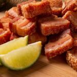 Imagem de uma tábua de madeira com uma porção de torresmo e meio limão cortado