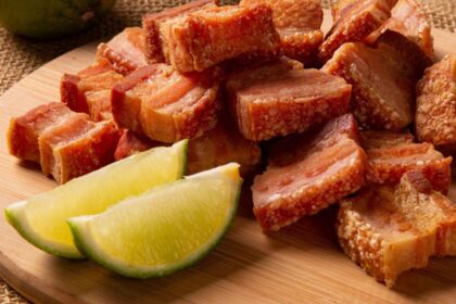 Imagem de uma tábua de madeira com uma porção de torresmo e meio limão cortado