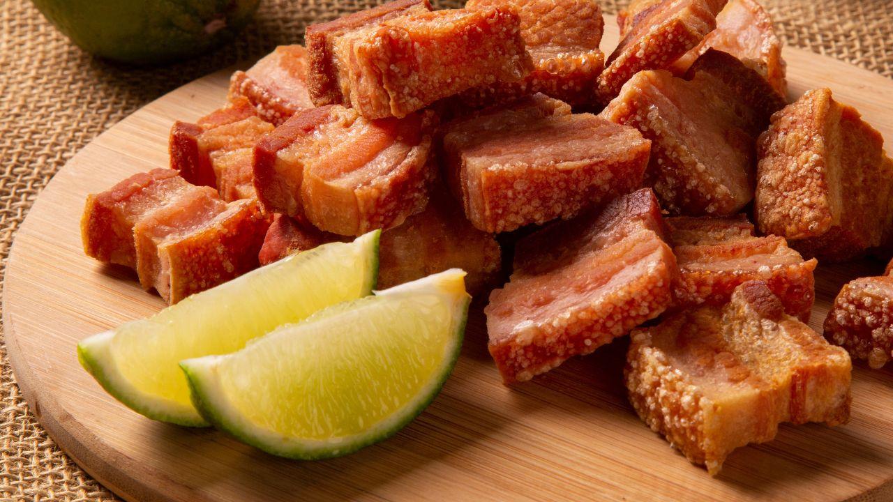 Imagem de uma tábua de madeira com uma porção de torresmo e meio limão cortado