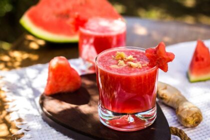 Foto mostra copo de drink de melancia em cima da mesa ao ar livre.