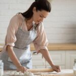 Mulher fazendo massa em cima da mesa.