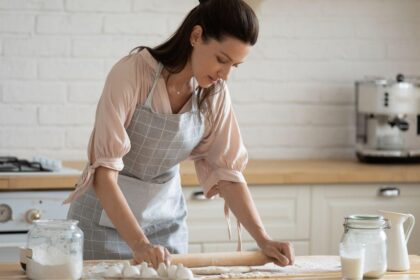 Mulher fazendo massa em cima da mesa.