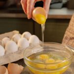 Imagem de uma pessoa quebrando ovos em um recipiente de vidro