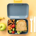 Comida na lancheira. Pão, fruta e água em cima da mesa.