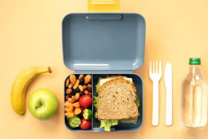 Comida na lancheira. Pão, fruta e água em cima da mesa.
