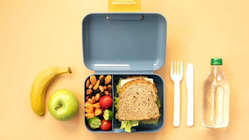 Comida na lancheira. Pão, fruta e água em cima da mesa.
