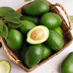 Foto mostra abacates dentro de uma cesta em cima da mesa.