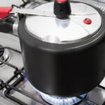 Foto mostra uma panela de pressão no fogo em cima do fogão aceso.