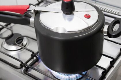 Foto mostra uma panela de pressão no fogo em cima do fogão aceso.