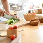 Mulher cortando alimentos em uma tábua em cima de uma mesa.