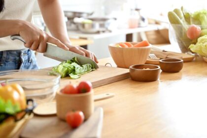 Mulher cortando alimentos em uma tábua em cima de uma mesa.