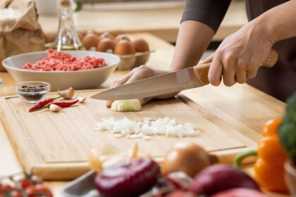 Foto mostra mulher cortando legumes na tábua.