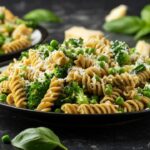 Foto mostra macarrão parafuso colorido com queijo em cima dentro de um prato em cima da mesa.