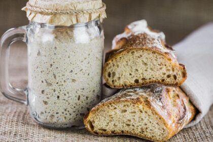 Foto mostra o levain dentro de um frasco ao lado de um pão caseiro.