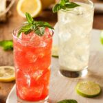 Foto mostra copos de drinks coloridos em cima de uma mesa.