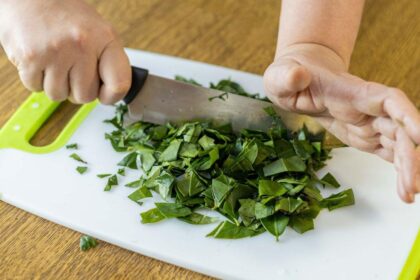 Planta verde sendo cortada em pedacinhos numa tábua em cima da mesa.