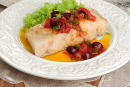 Foto mostra um pedaço de bacalhau com tomates e alface em um prato.