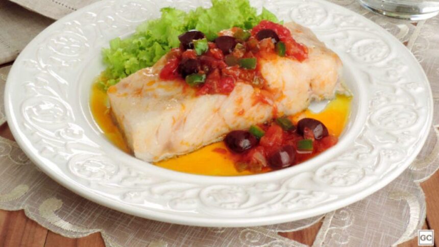 Foto mostra um pedaço de bacalhau com tomates e alface em um prato.