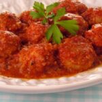 Foto mostra almôndegas com molho em um prato branco em cima da mesa.