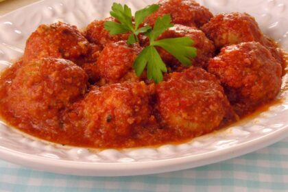 Foto mostra almôndegas com molho em um prato branco em cima da mesa.